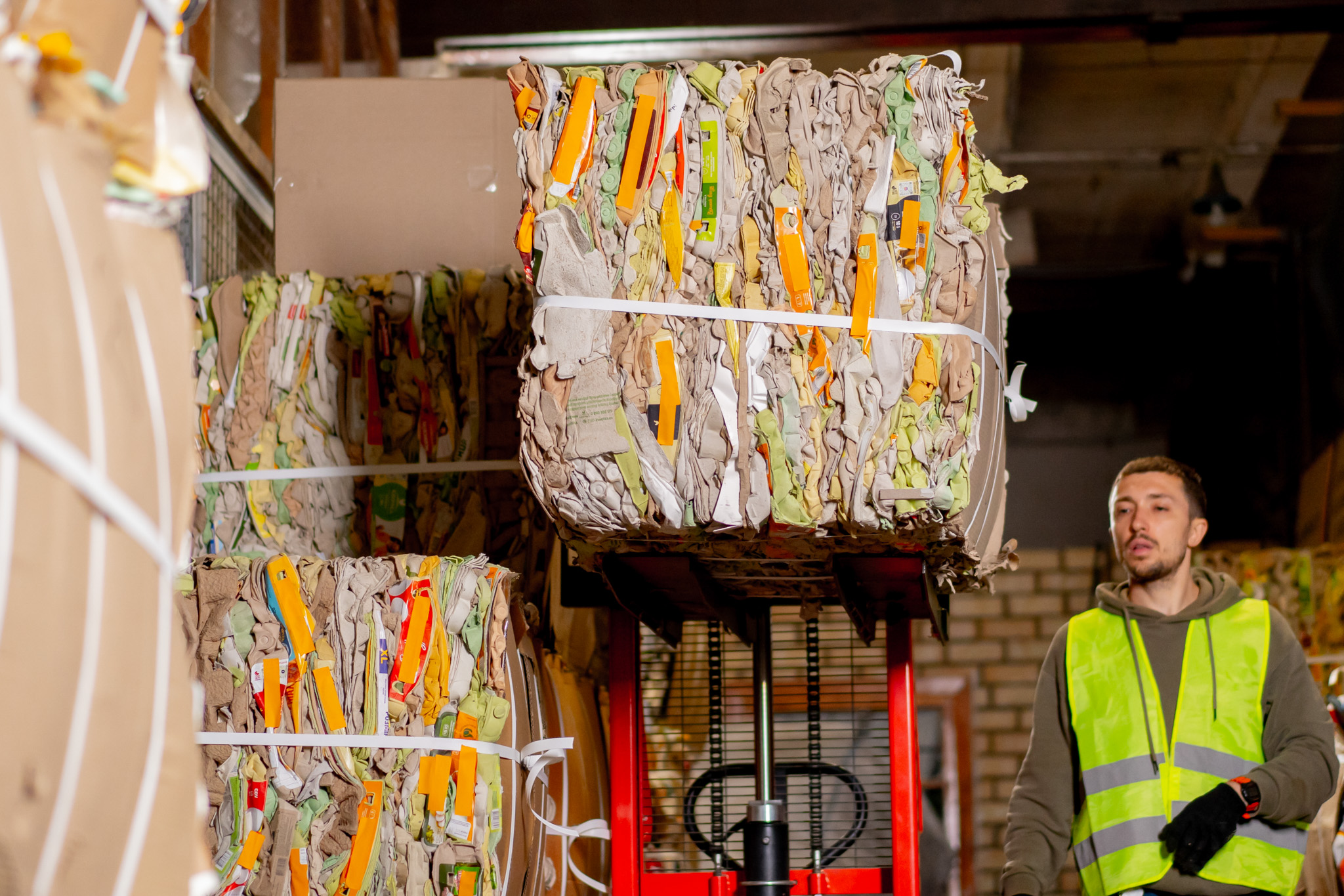 Worker operating a forklift to manage compressed packaging waste at a recycling facility.